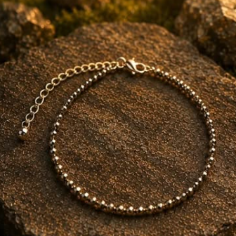 A silver beaded anklet with a matching chain extender and lobster clasp, displayed on a textured brown rock outdoors.