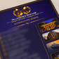 A close-up angled view of a glossy dark blue brochure or booklet cover with gold trim, featuring the text 'Millionaires Mind Hub' and 'Affirmations Board,' plus small inset photos of luxurious buildings and a yacht.