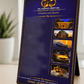 A vertical framed affirmation board standing on a tabletop in a real indoor setting. The board has a dark navy to black gradient background with gold decorative border lines, gold logo text reading 'Millionaires Mind Hub Affirmations Board,' and four inset photos showing a building at night, a yacht, a gold car, and cash.