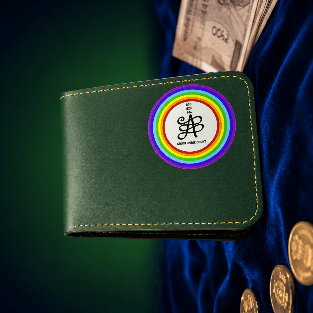 A dark green leather wallet with a circular rainbow logo featuring the text 'BANKER'S ASS' and 'EST. 2015', displayed on a dark blue velvet surface with gold coins and a banknote nearby.