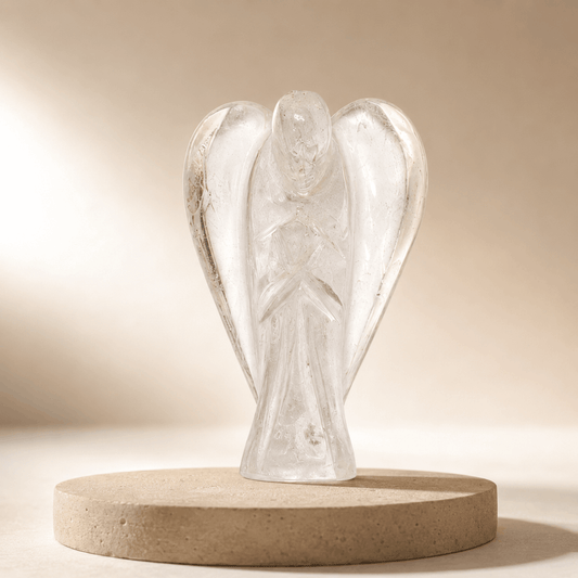 A clear glass angel figurine standing on a round beige stone base against a warm beige background.