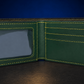 A dark green leather bifold wallet shown open, featuring bright yellow contrast stitching, a clear ID window on the left, and card slots on the right, set against a dark blue background.