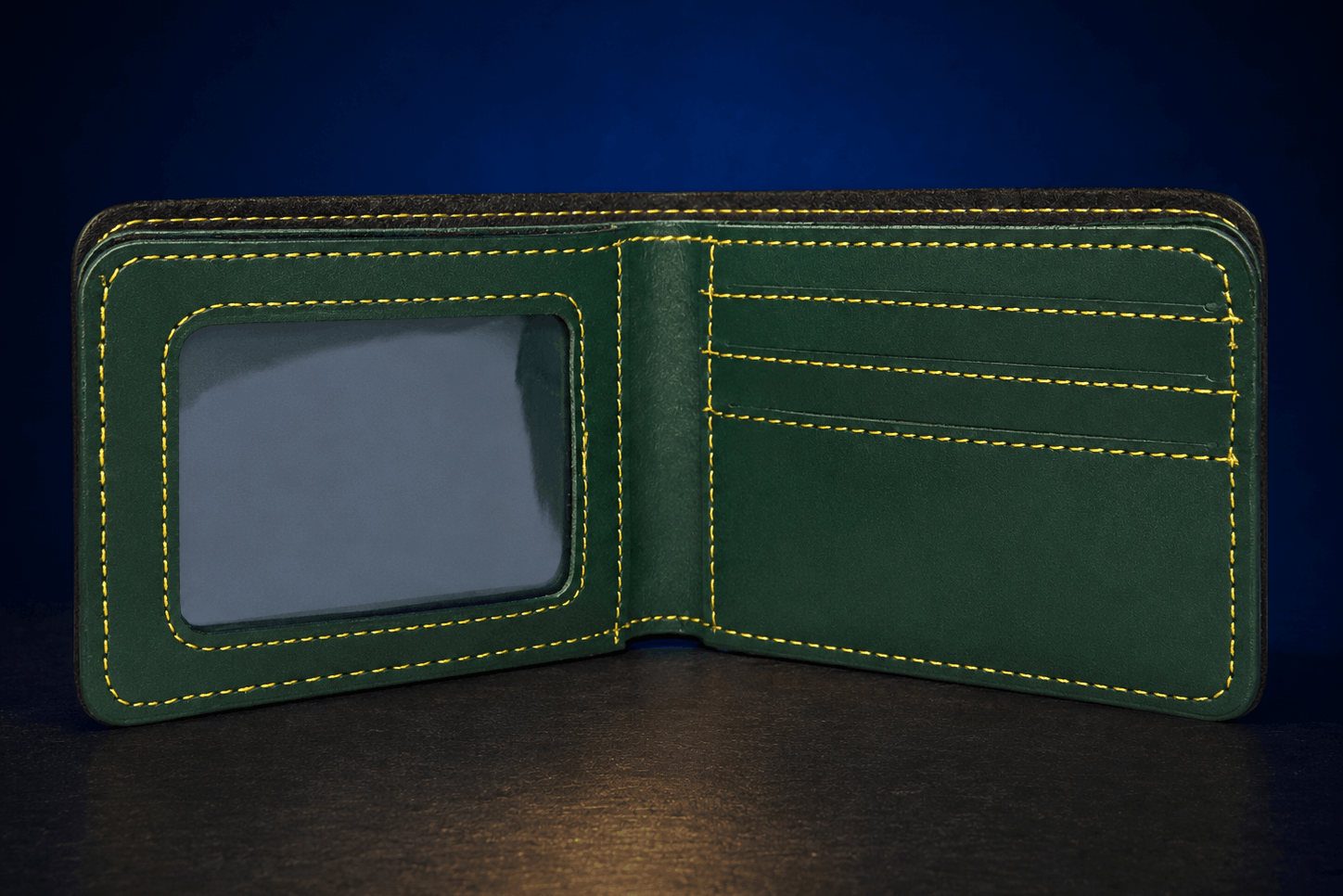 A dark green leather bifold wallet shown open, featuring bright yellow contrast stitching, a clear ID window on the left, and card slots on the right, set against a dark blue background.