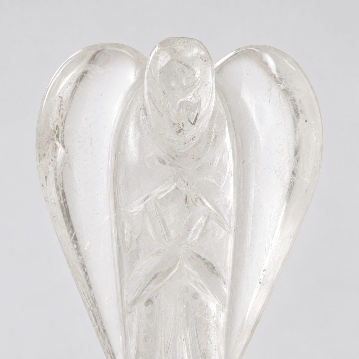 A clear glass angel figurine with detailed wings and a carved face, shown against a neutral light gray background.