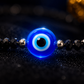 Blue evil eye bead on a black beaded bracelet with a blurred background