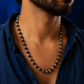 Man wearing a black beaded necklace against a blue background