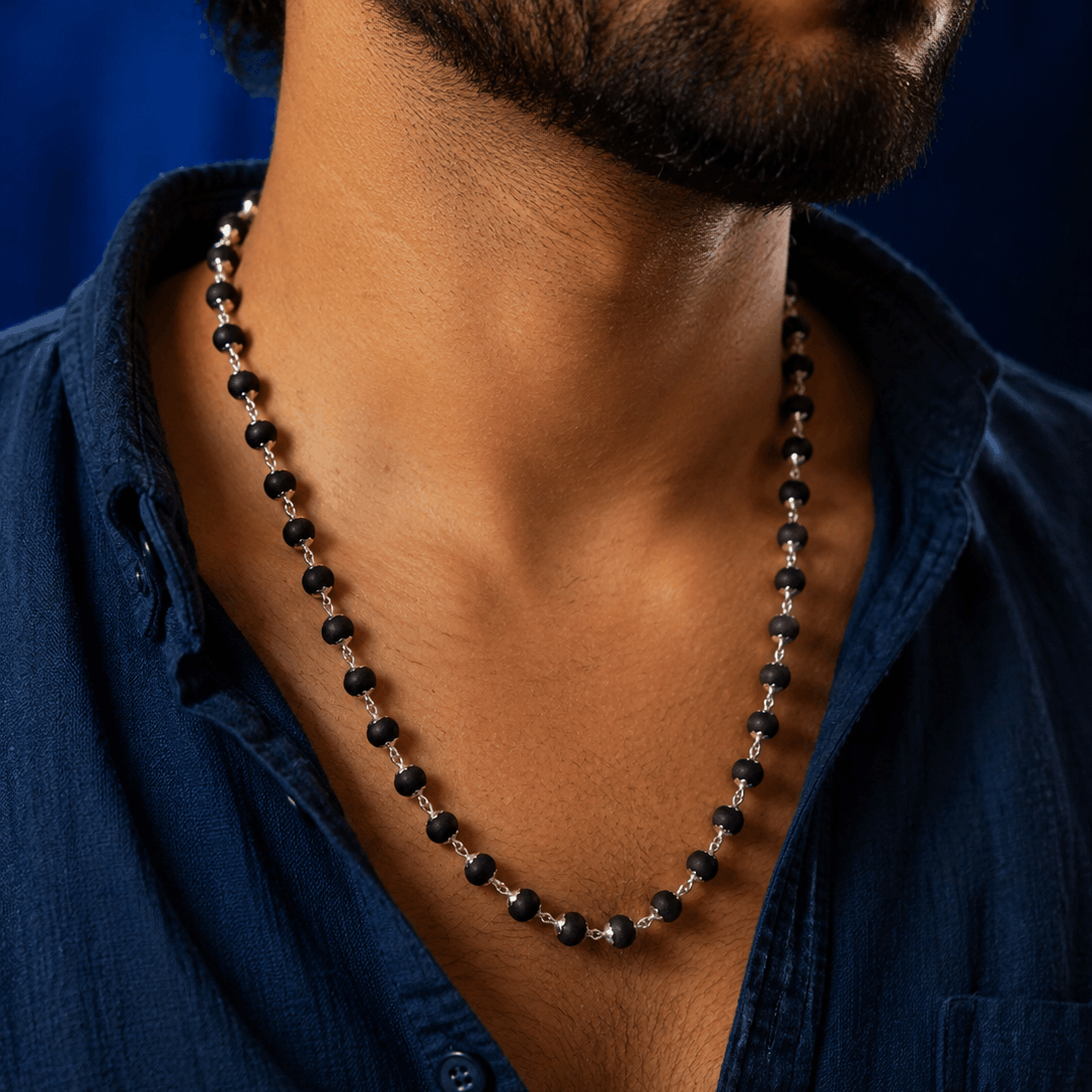Man wearing a black beaded necklace against a blue background
