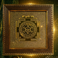 Decorative panel with a geometric design in a wooden frame, surrounded by candles and flowers on a dark background.