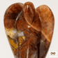 A polished carved stone sculpture of an angel with wings, featuring natural marbled patterns in warm brown, amber, and translucent white, set against a plain light gray background.