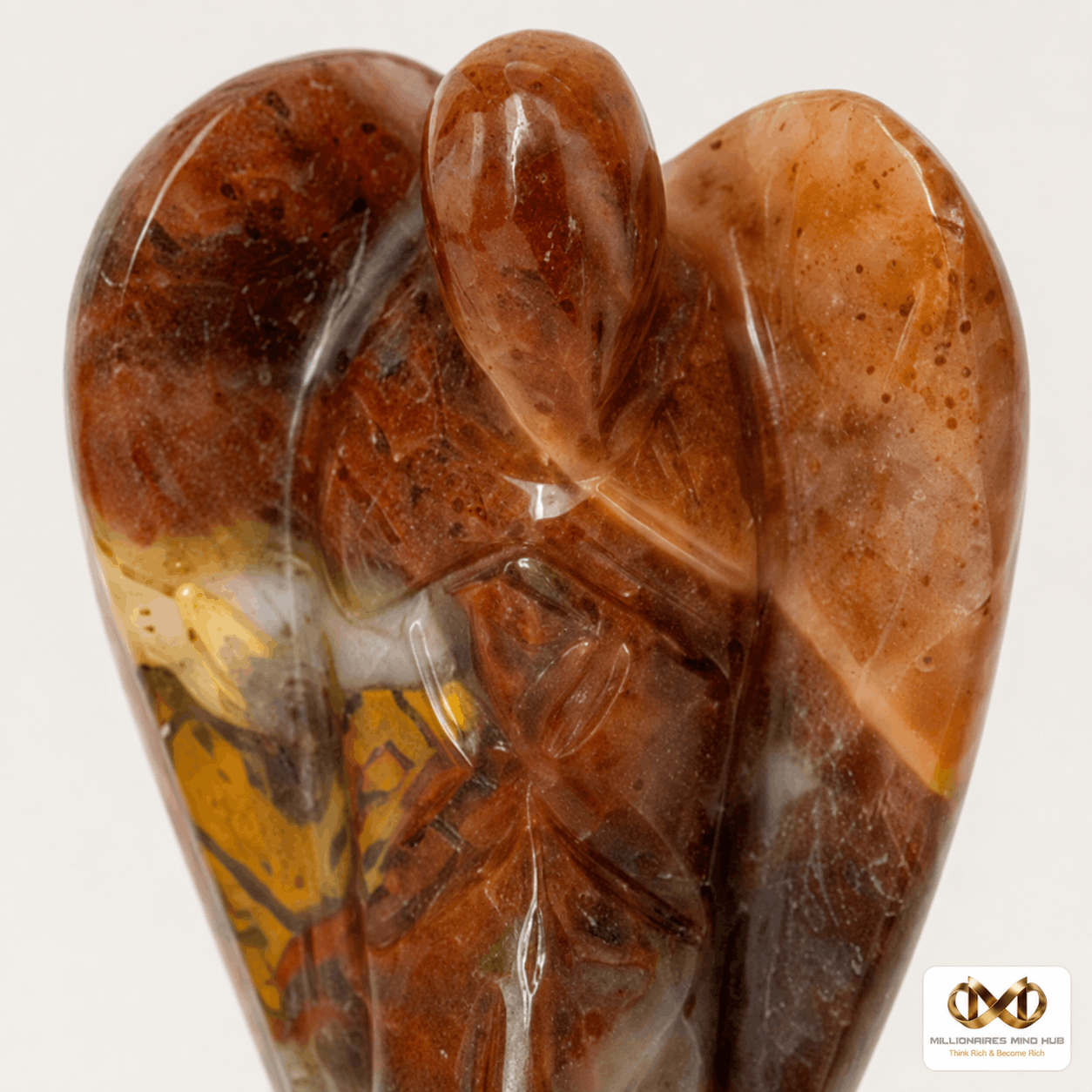 A polished carved stone sculpture of an angel with wings, featuring natural marbled patterns in warm brown, amber, and translucent white, set against a plain light gray background.
