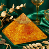 Decorative pyramid with a spiral design on a green fabric background with gold leaves and a glass.