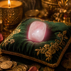Pink crystal on a green embroidered pillow with gold coins and a lit candle in the background