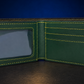 An open dark green leather bifold wallet with bright yellow contrast stitching, featuring an ID window on the left and card slots on the right, set against a dark blue background.