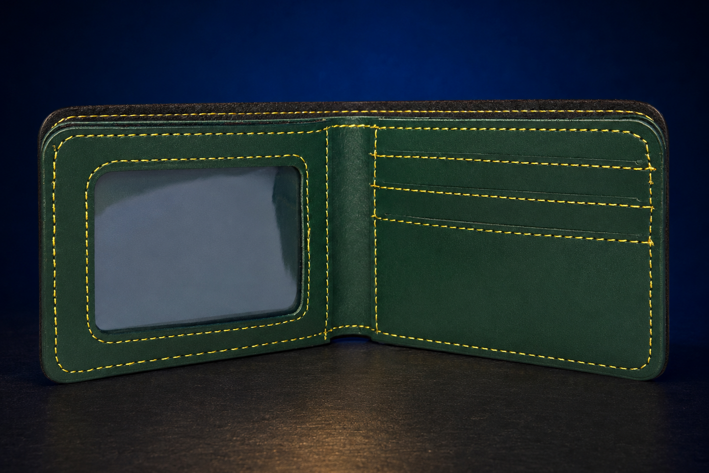 An open dark green leather bifold wallet with bright yellow contrast stitching, featuring an ID window on the left and card slots on the right, set against a dark blue background.