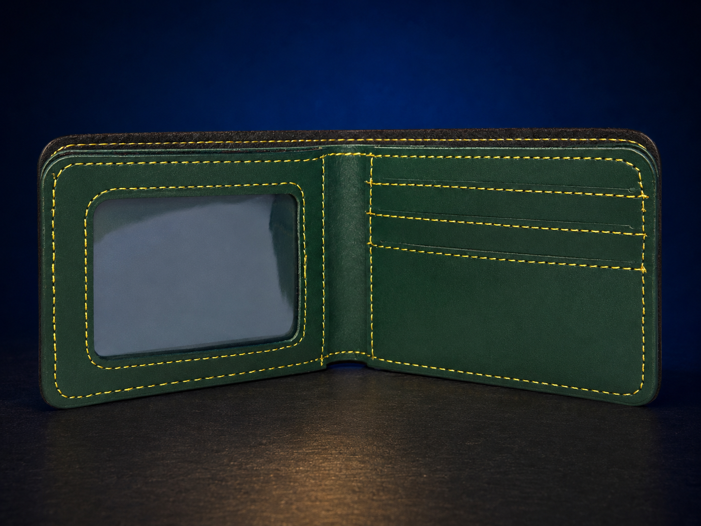 An open dark green leather bifold wallet with bright yellow contrast stitching, featuring an ID window on the left and card slots on the right, set against a dark blue background.