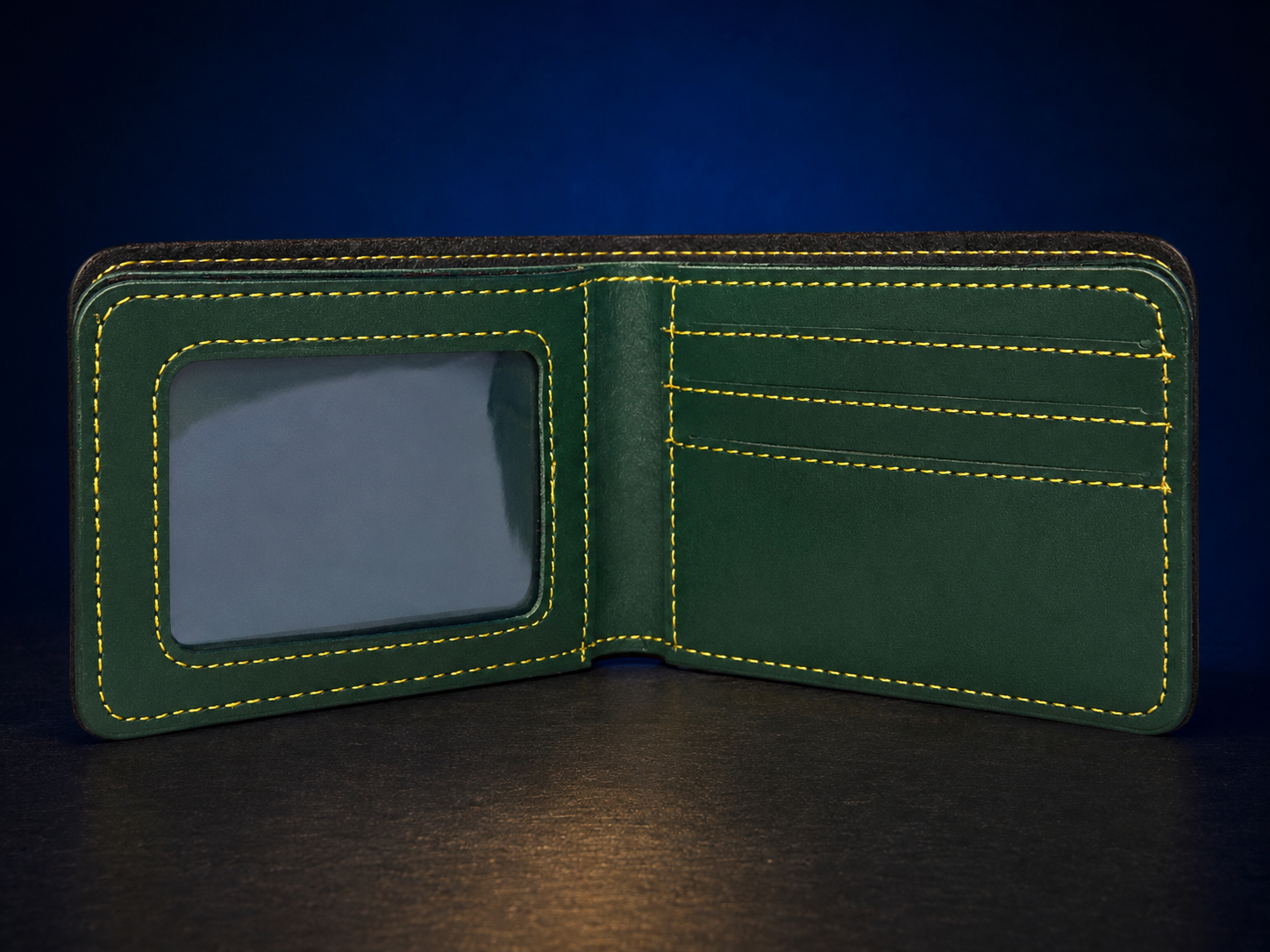 An open dark green leather bifold wallet with bright yellow contrast stitching, featuring an ID window on the left and card slots on the right, set against a dark blue background.