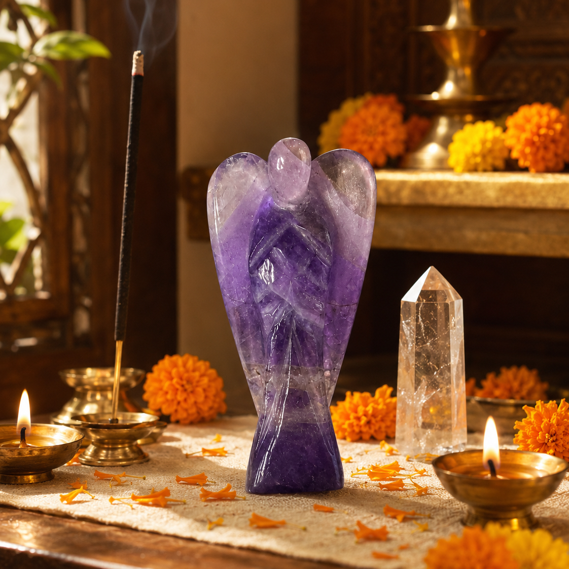 A purple amethyst angel statue stands on a wooden altar surrounded by lit brass oil lamps, a smoking incense stick holder, a clear crystal point, and orange marigold flowers.