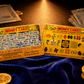 Two gold 'Money Card' with text and symbols on a blue fabric background with money and coins.