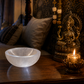 Decorative setting with a crystal bowl, statue, and candle on a table in a room with a window view of the moon.