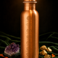 Copper water bottle with engravings on a dark background with crystals and leaves