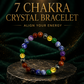 A 7 chakra crystal bracelet made of multicolored polished gemstone beads, displayed on a dark textured stone pedestal against a dark green velvet background with gold text overlays.