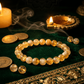 Bracelet with gold beads on a dark surface with candles and coins