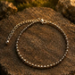 A silver beaded anklet with a matching chain extender and lobster clasp, displayed on a textured brown rock outdoors.